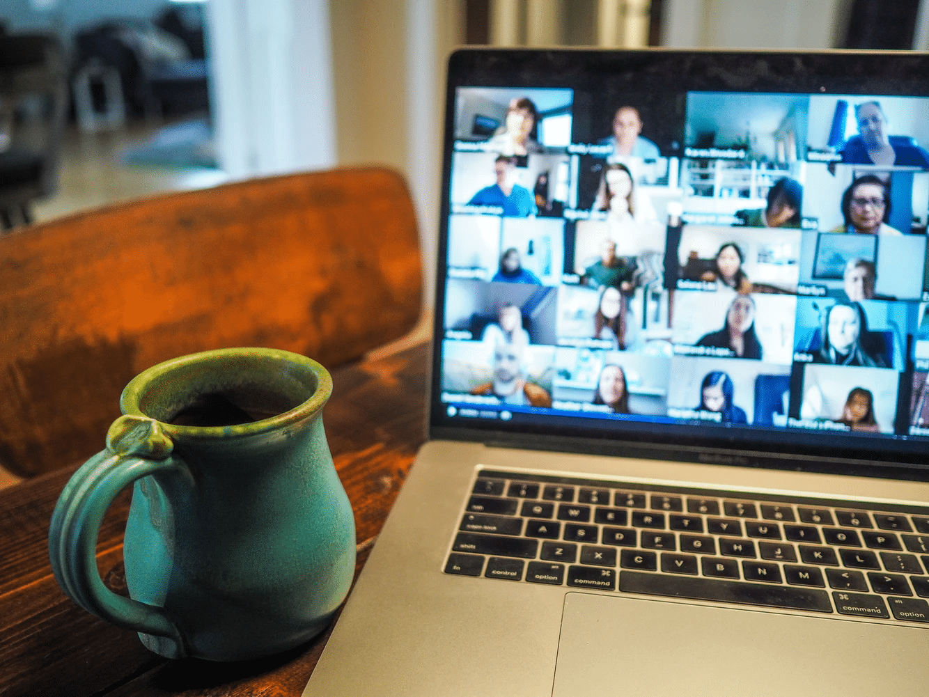 A mug next to an open laptop displaying a Zoom meeting filled with participants.