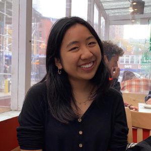Lily Lou, the author, smiles at the camera in the middle of a coffeeshop.