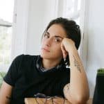 Liana DeMasi props their face up with their elbow, looking at the camera seriously.