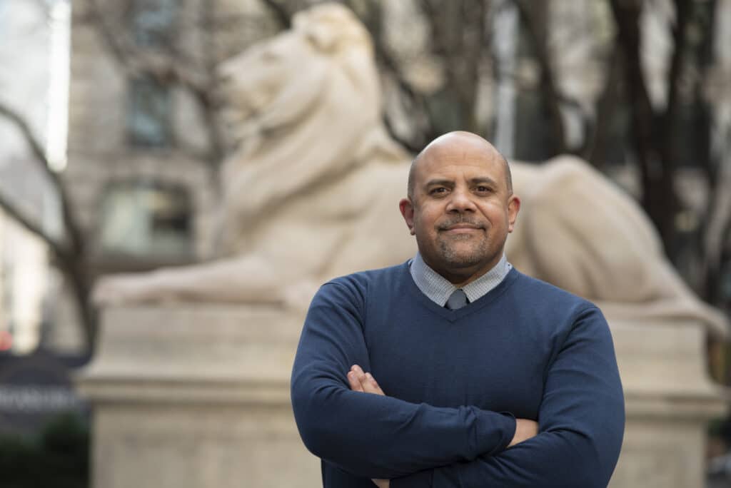 Dr. Thrasher stands in front of a lion sculpture with his arms crossed.
