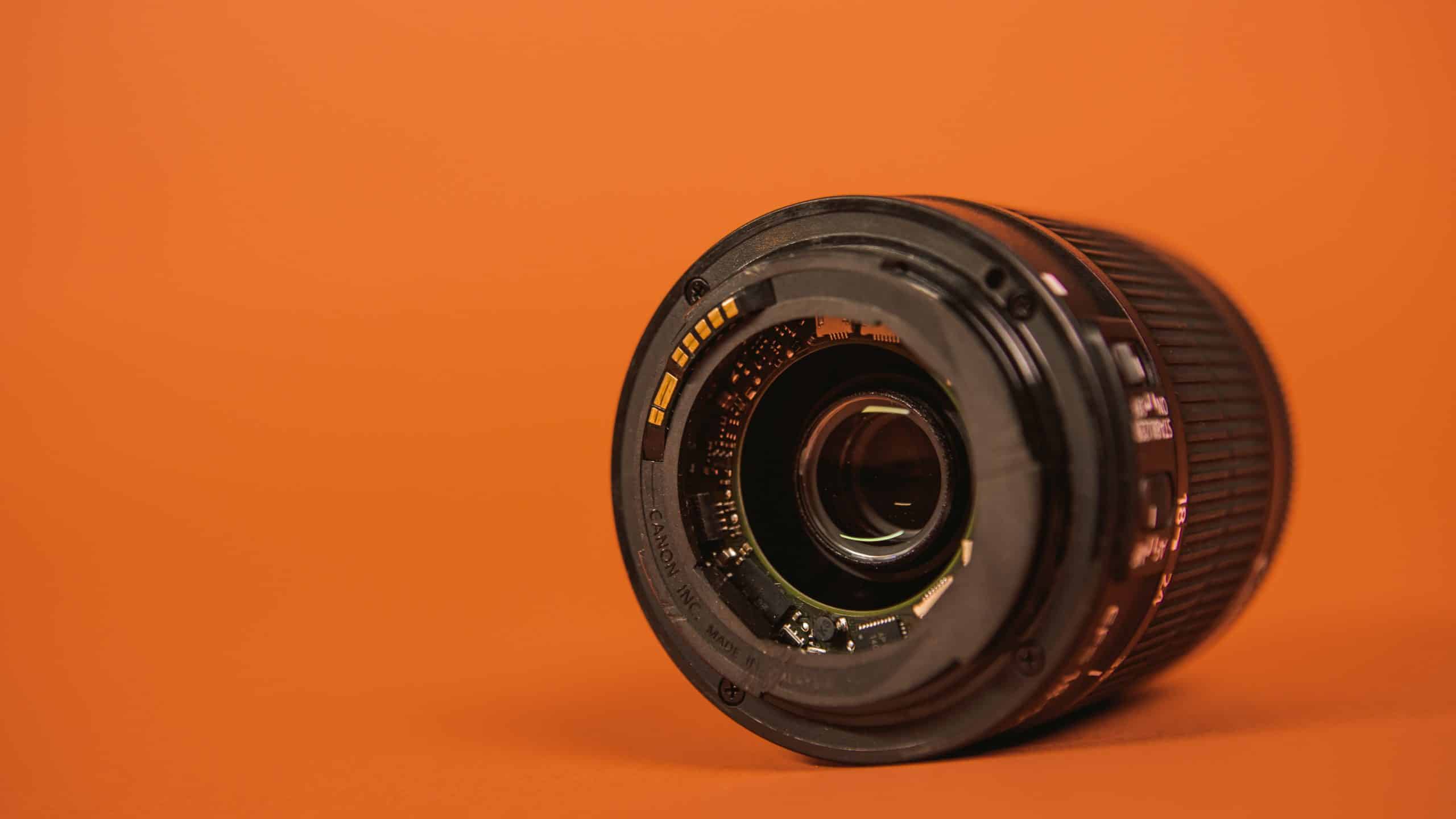 A broken camera lens on an orange backdrop.