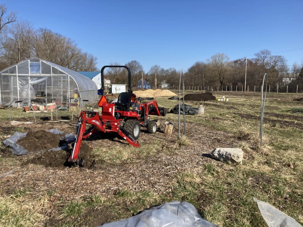 A red tractor on the fields of Brady Farm, in front of greenhouses.