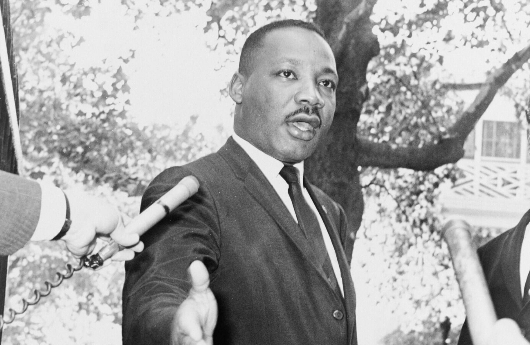 A black and white photo of Rev. Martin Luther King Jr. speaking to two microphones pointed at his face.