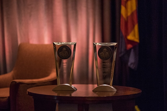 Two clear glass awards dedicated to Gwen Ifill and Judy Woodruff are on a wooden table.