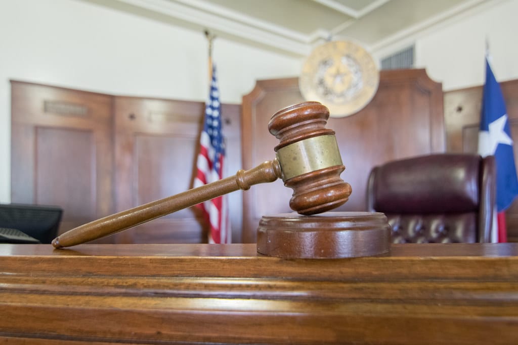 A gavel perched in front of an empty courtroom bench.