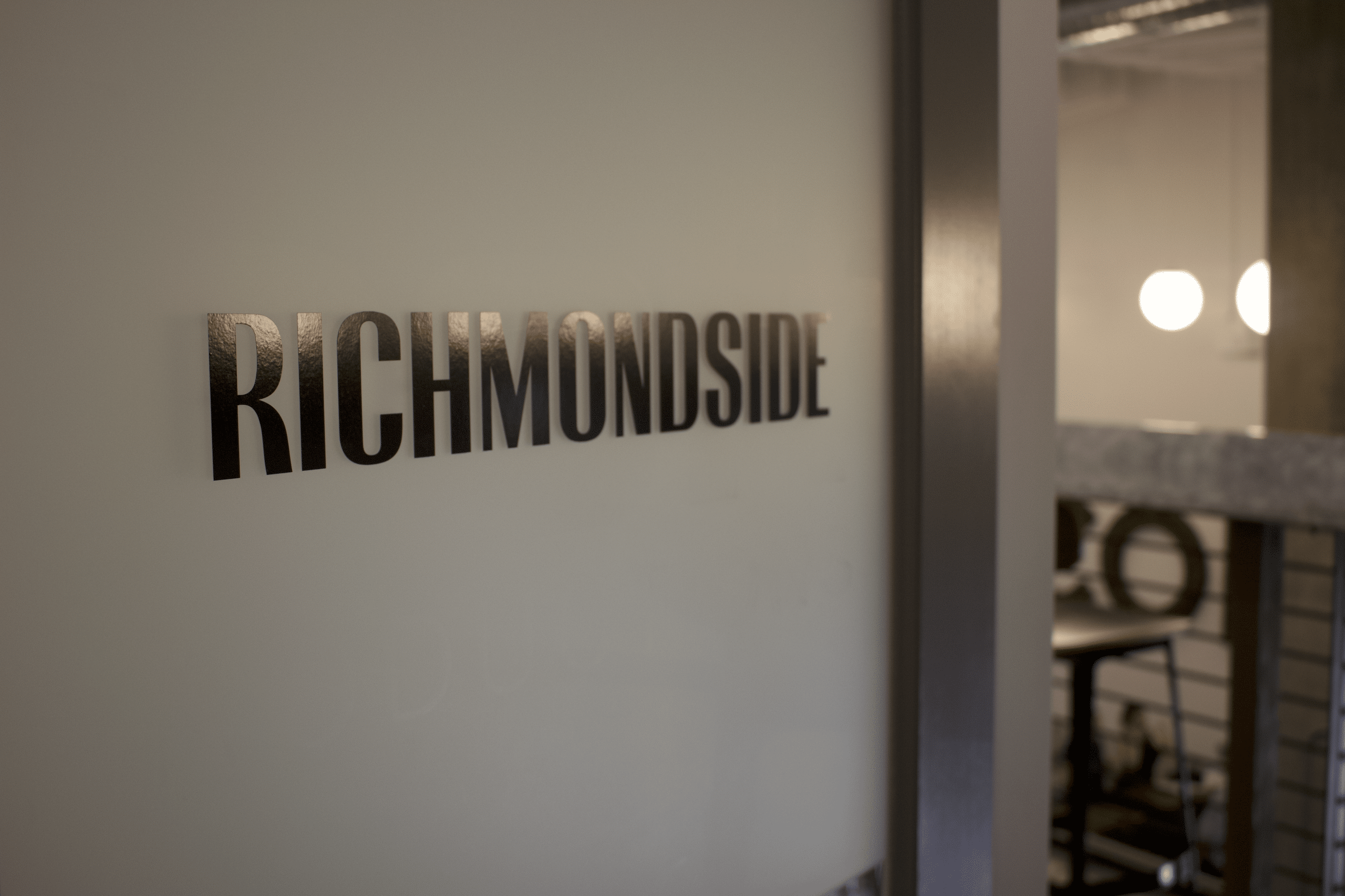 Bronze, sans-serif all-capital letters read Richmondside next to the entryway to the Richmondside newsroom.