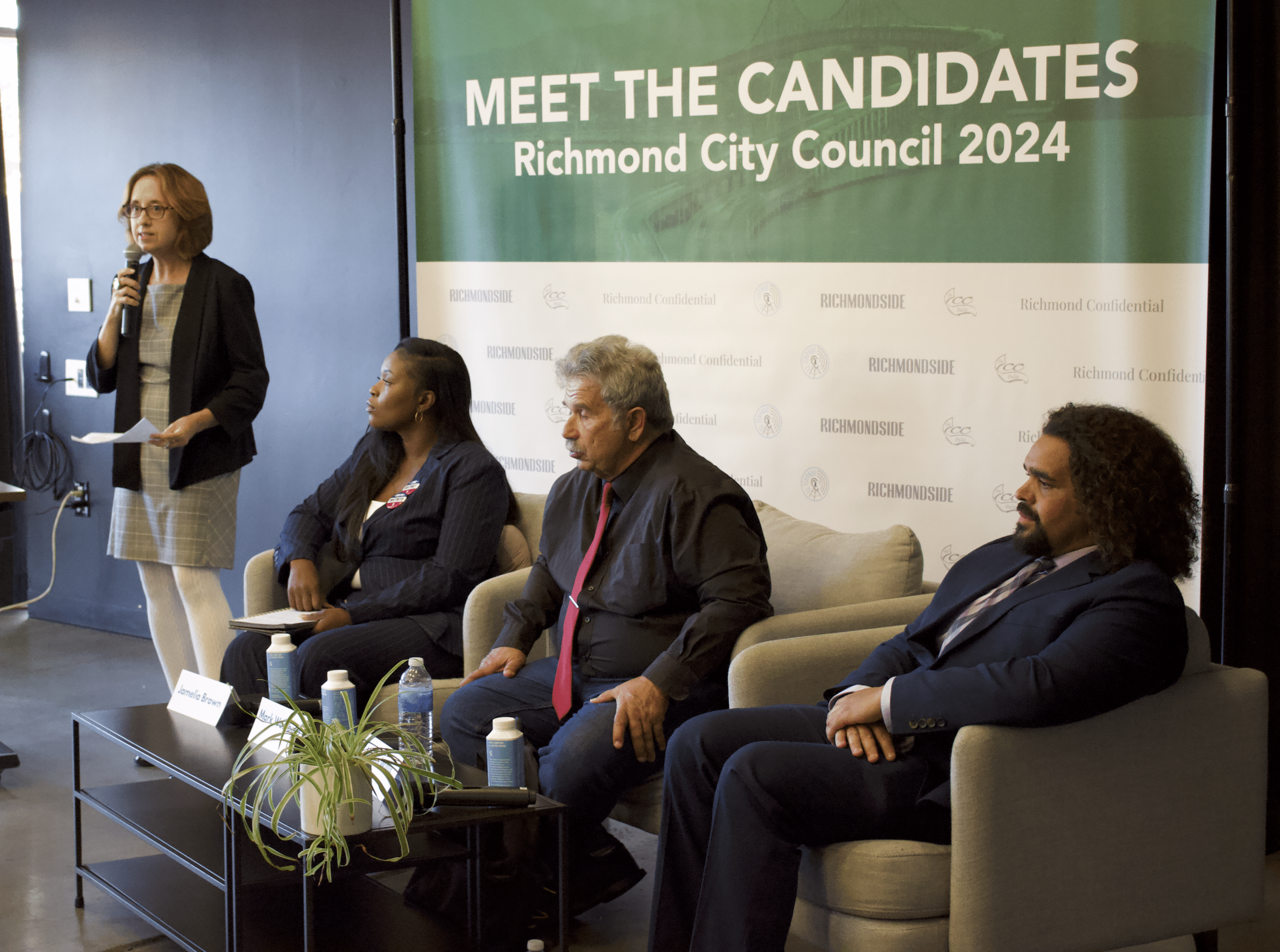Richmondside editor-in-chief Kari Hulac introduces Richmond City Council District 1 candidates Jamelia Brown, Mark Wassberg, and Melvin Willis in front of a Meet The Candidates [for] Richmond City Council 2024 banner. 