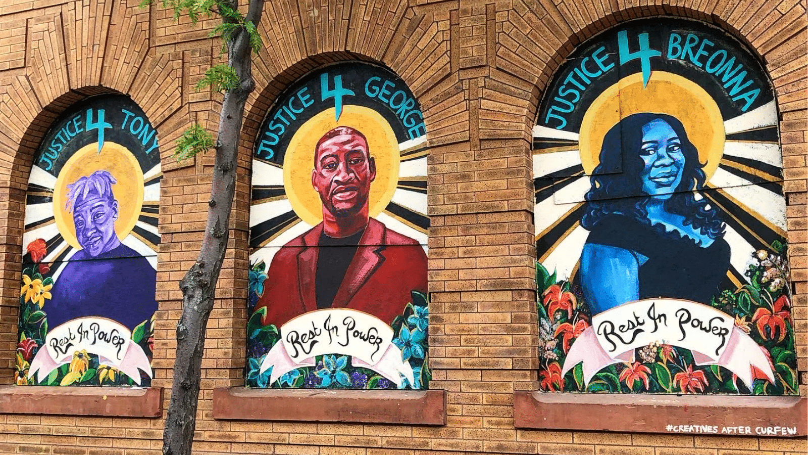 A mural in Minneapolis, Minnesota depicting three Black Americans who were killed by police officers in 2020. From left to right, they are Tony McDade, George Floyd, and Breonna Taylor. Each person is framed by flowers, a banner that reads "Rest in Power", a sun, and language that says "Justice 4 Tony", "Justice 4 George", and "Justice 4 Breonna", respectively.